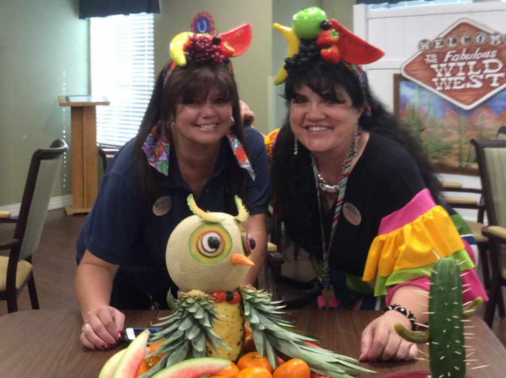 Pegasus Landing of Mesa | Teresa Hadley smiling with her coworker behind sculpted fruit