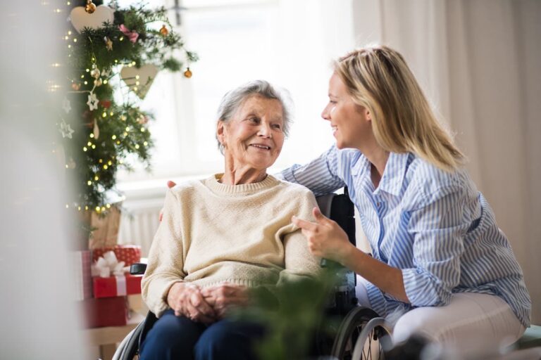 Pegasus Landing of Mesa | Smiling senior woman with caregiver sitting beside the Christmas tree