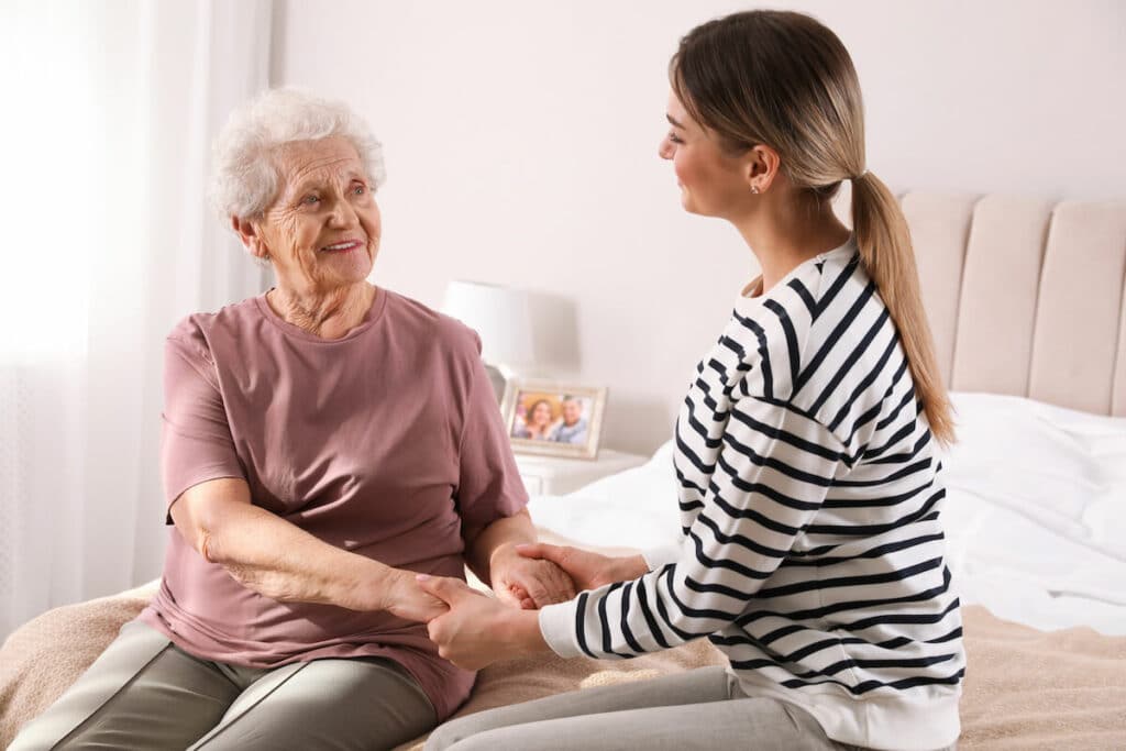 Pegasus Landing of Overland Park | Senior woman and her caregiver sitting on a bad holding hands