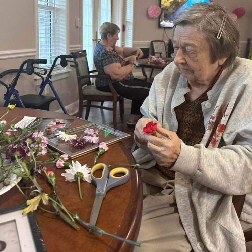 Pegasus Landing of Overland Park | Senior woman creating floral craft in room of other crafters