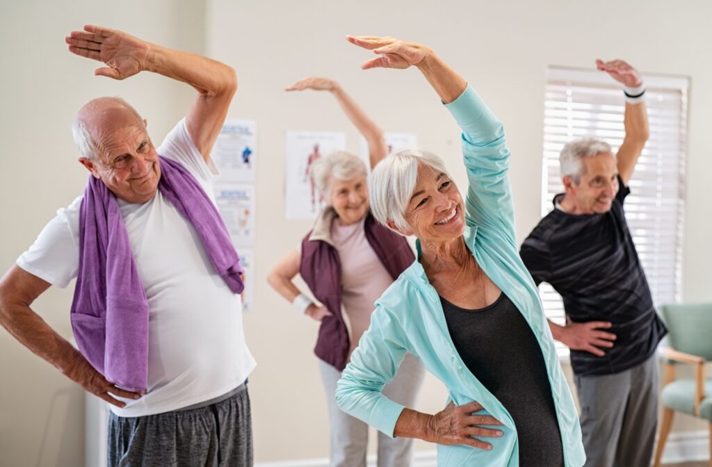 The Legacy At Falcon Point |  A group of older adults in an exercise class smiling and stretching with one hand over their heads