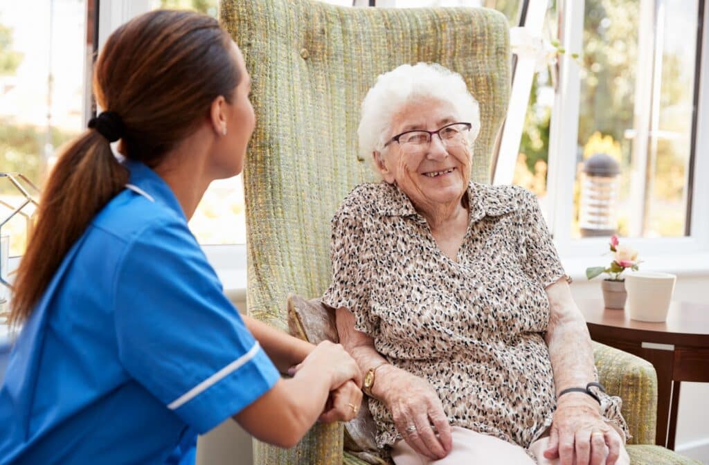 The Legacy At Falcon Point |  An older adult woman in a senior living community sitting on a chair and smiling while having a conversation with a staff member