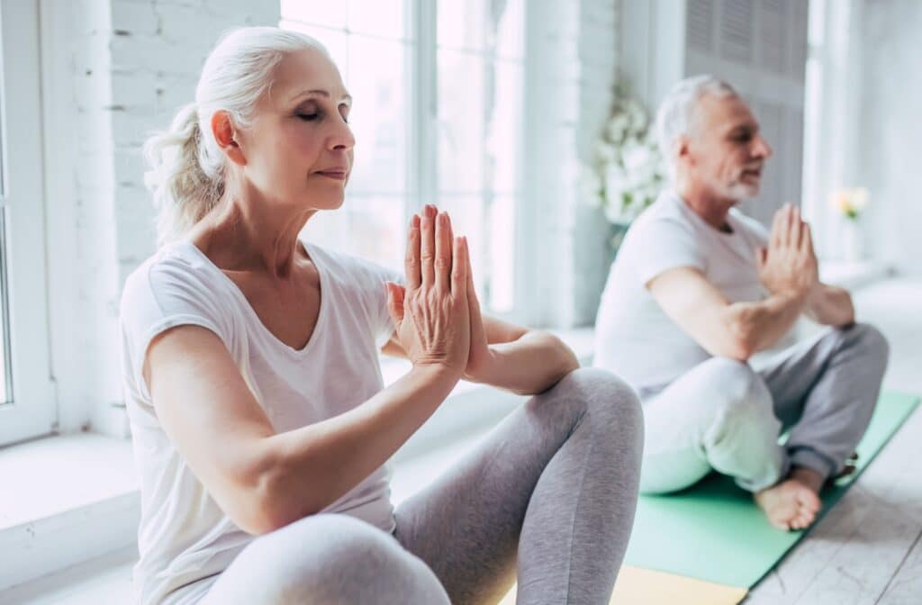 The Legacy At Falcon Point | 2 seniors with closed eyes practicing yoga and sitting on yoga mats