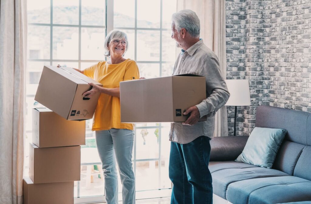 The Legacy At Falcon Point | An older adult couple carries moving boxes into their new home and shares a smile.