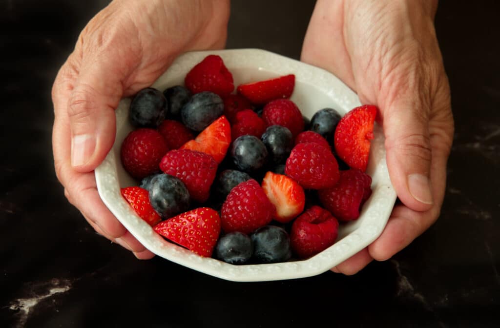 The Legacy At South Plains | A senior woman's hands holding a bowl of blueberries and strawberries.