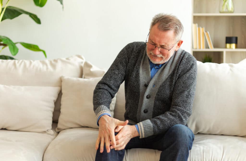 The Legacy At South Plains | An older adult man sitting on a couch and holding his right knee due to pain