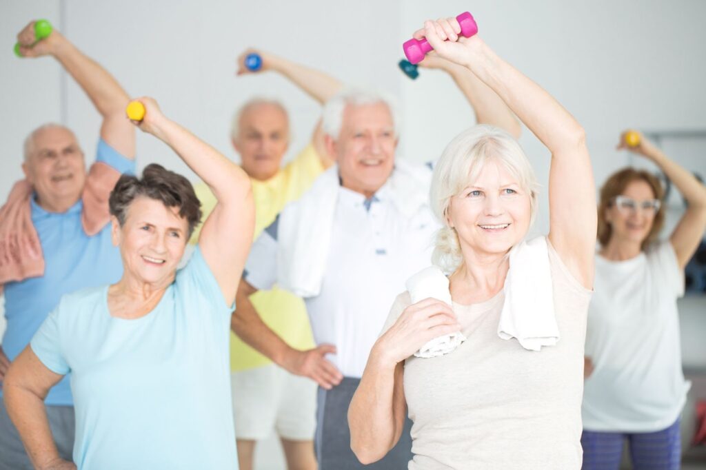 The Legacy At South Plains | The Older adults in a group class smiling and exercising with dumbbells.